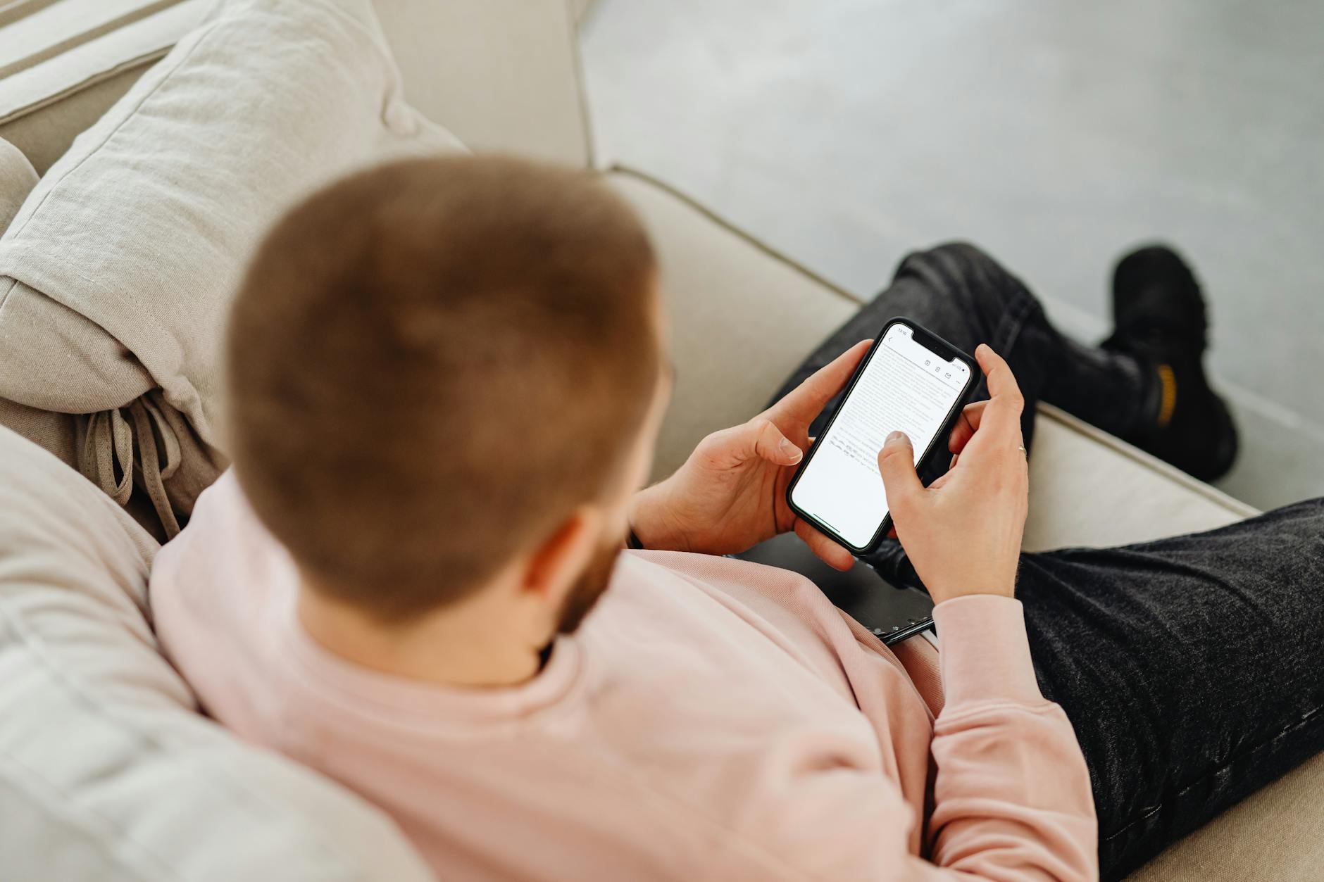 a man sitting on sofa holding black smartphone
